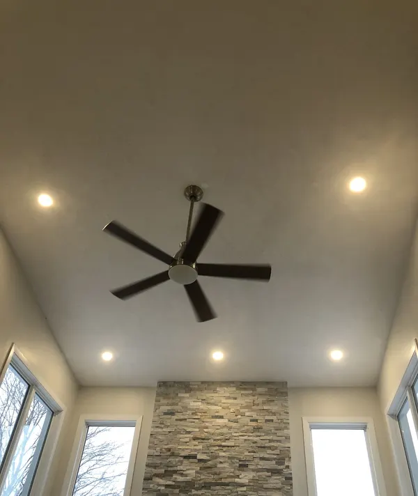 Looking up at a ceiling fan and four pot lights above a stone feature wall.