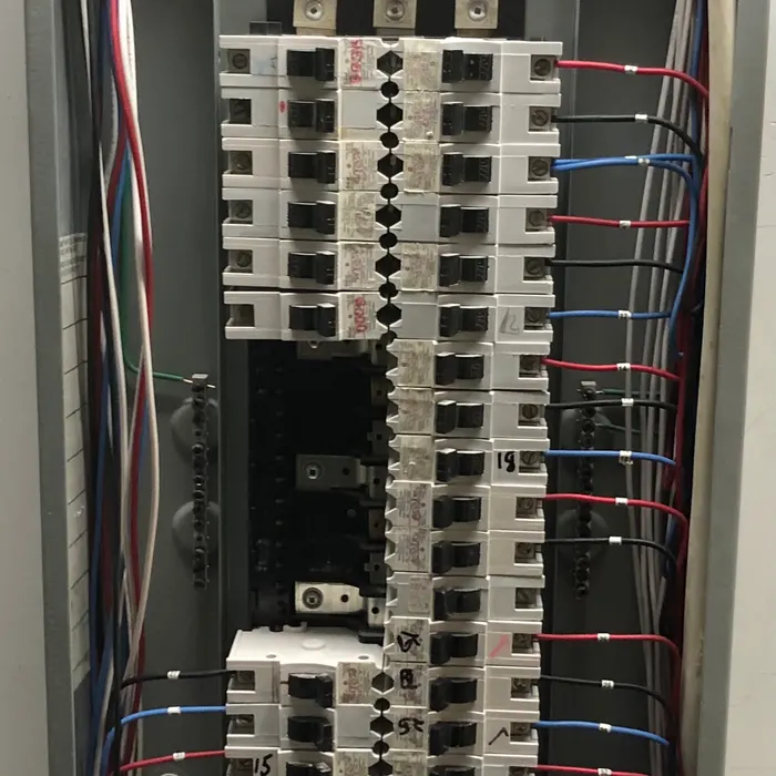 Inside an electrical panel: two columns of breakers with coloured wires running to each one.